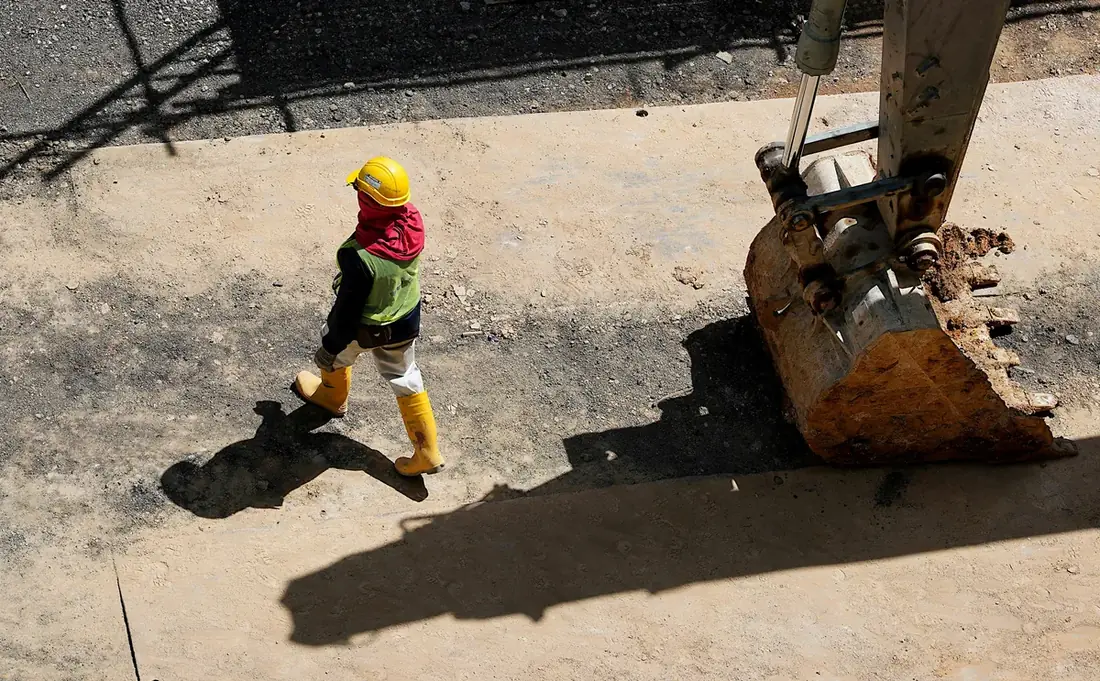 Construction worker walking past an excavator bucket on site